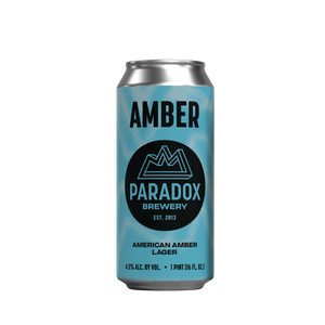 A single aluminum beer can for Paradox Brewery's Amber American Amber Lager, featuring a light blue and teal patterned design with a black circular logo, centered on a plain white background.