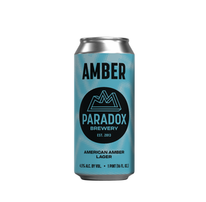 A single aluminum beer can for Paradox Brewery's Amber American Amber Lager, featuring a light blue and teal patterned design with a black circular logo, centered on a plain white background.