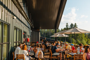 People dining outdoors at a restaurant with trees in the background at Paradox Brewery